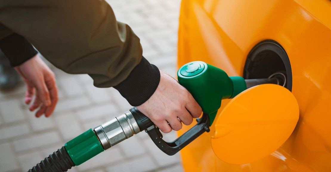 Άνδρας με χακί μπουφάν κρατά πράσινη αντλία βενζίνης και γεμίζει βενζίνη σε πορτοκαλί αμάξι