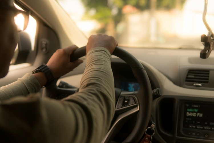 Χέρια άνδρα οδηγού κρατούν τιμόνι αυτοκινήτου.