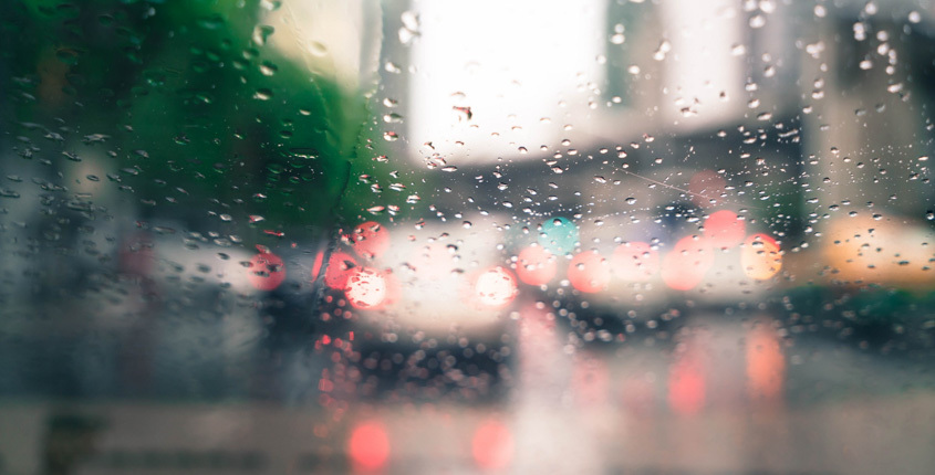 Θολό τζάμι αυτοκινήτου με σταγόνες βροχής και μπροστά φώτα αυτοκινήτων.